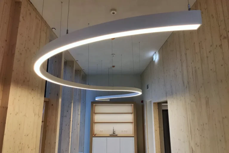 Büroraum mit Wänden aus hellem Holz, geschwungener LED-Leuchte und Einbauregal in Eupen