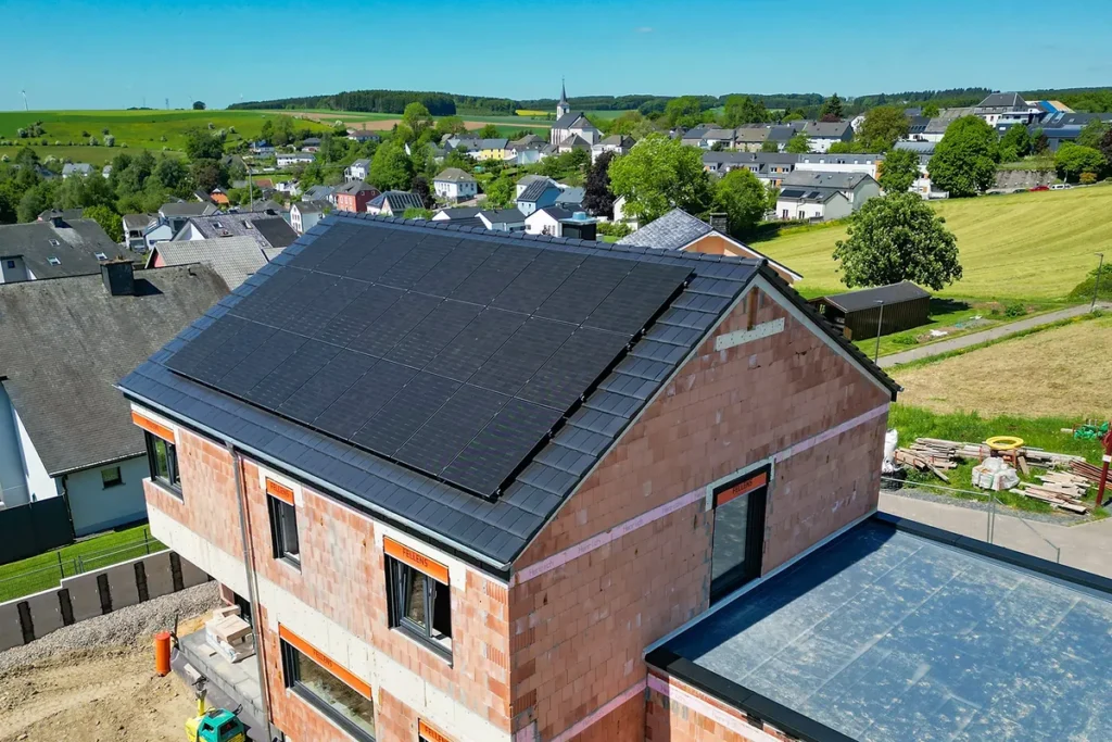 Rohbau aus rotem Mauerwerk mit dunklem Ziegeldach und Photovoltaikmodulen, Luftaufnahme