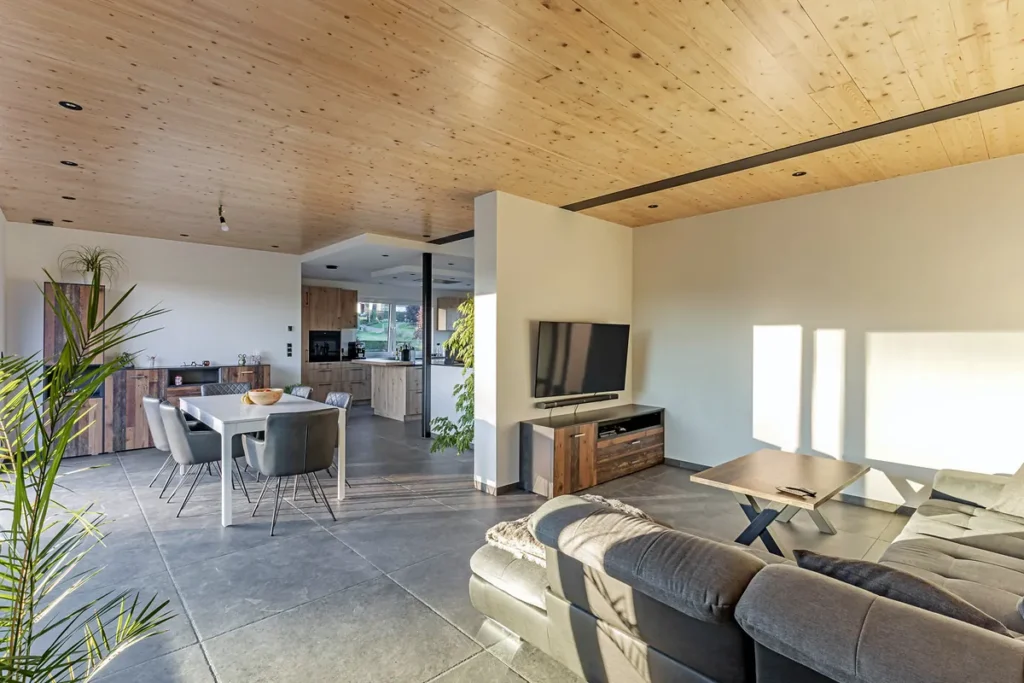 Offener Wohn- und Essbereich mit Holzdecke, grauem Fliesenboden, Sofa und Esstisch