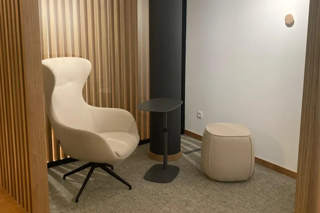 Sitznische im Büro mit Holzlamellen, hellem Sessel und kleinem Beistelltisch