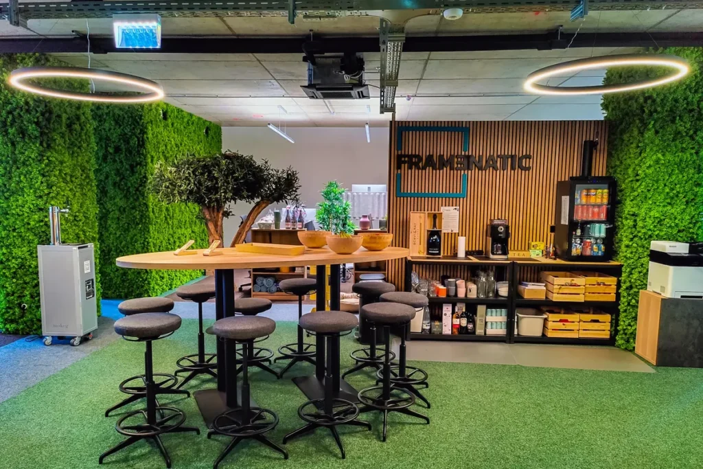 Caféecke im Büro mit Stehtisch, Hockern, Regal mit Kaffeemaschine und Mooswänden zu beiden Seiten