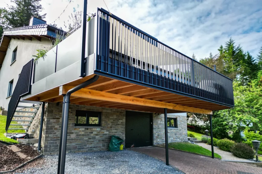 Erhöhte Terrasse mit schwarzem Geländer auf Stahlstützen, darunter Carport mit Holzuntersicht
