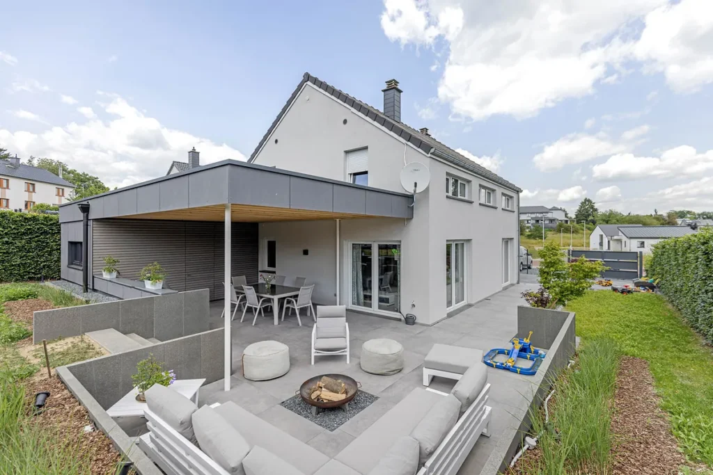 Einfamilienhaus mit überdachter Terrasse, Plattenbelag, Feuerschale, Lounge-Möbeln und Rasenfläche