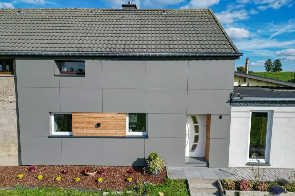 Hausfassade mit grauen Trespa-Platten, Holzakzent zwischen zwei Fenstern und Eingangstür