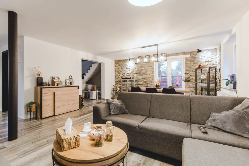 Wohnbereich mit Ecksofa und Couchtisch, dahinter Steinwand, Essplatz und Treppe