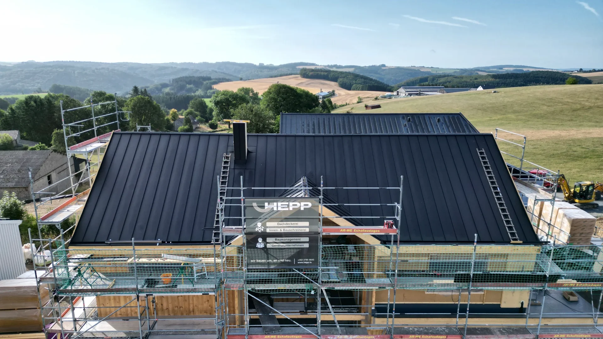 CLT-Holzhaus in Lieler im Bau: Satteldach mit Stehfalzdeckung in Anthrazit, am Gerüst das Bauschild von HEPP